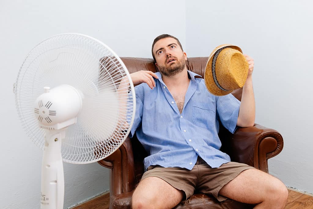man in front of fan, trying to cool down because AC is broken